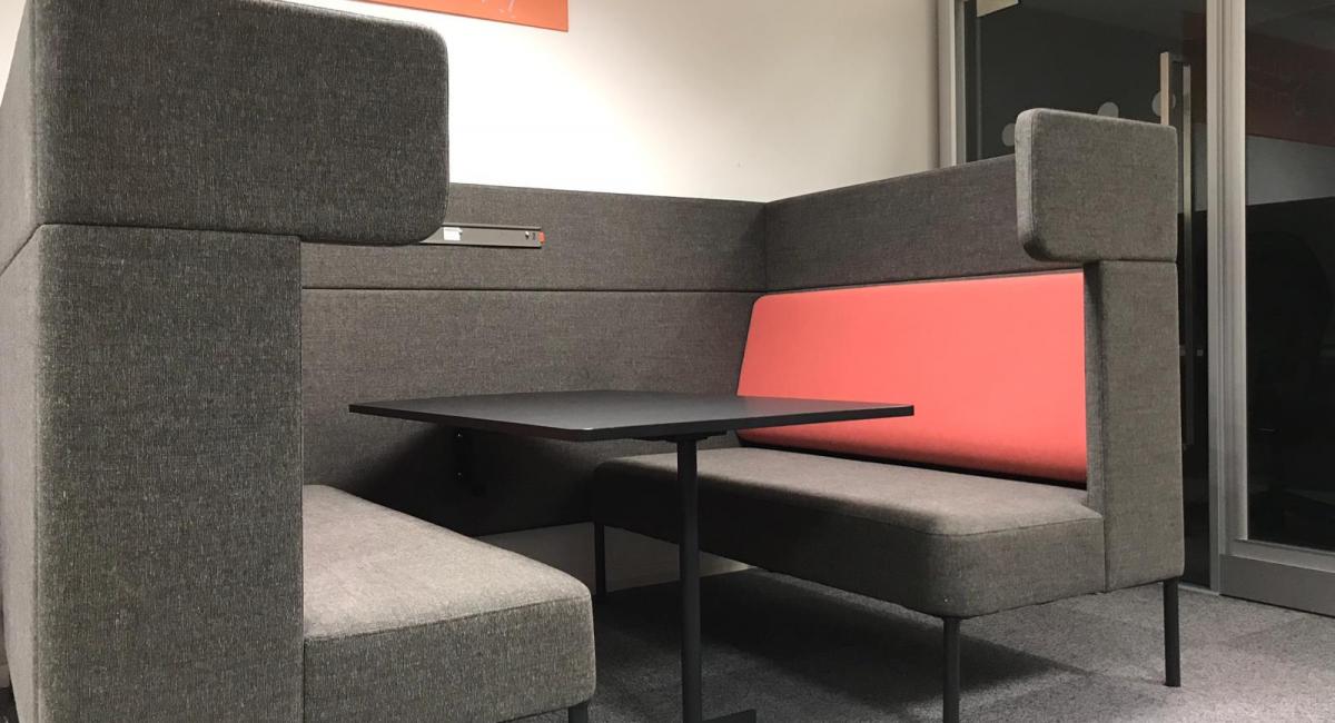 OCEE FourUS Work Booth upholstered in charcoal with red cushioning and black pivot table.