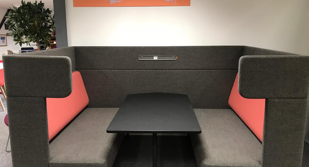 OCEE FourUS Work Booth upholstered in charcoal with red cushioning and black pivot table.