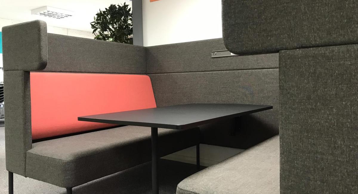 OCEE FourUS Work Booth upholstered in charcoal with red cushioning and black pivot table.