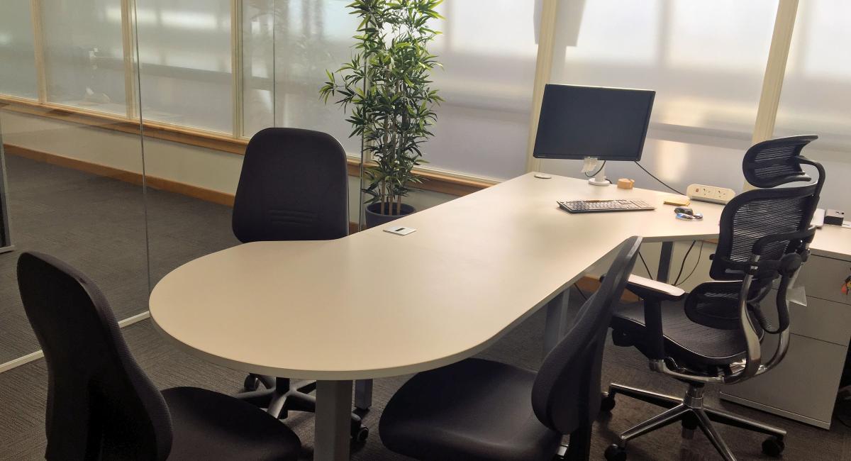 Office desk with consultation end and black upholstered task chairs.